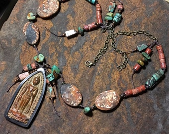 May include: A long necklace with a variety of stones, including turquoise, red, and brown. The necklace has a large pendant featuring a carved figure.