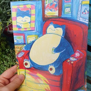 Op de afbeelding: Kleurrijke illustratie van een Snorlax-personage dat ontspant in een rode fauteuil, met een blikje in zijn hand. Het kunstwerk toont ingelijste foto's aan de muur en een gele en bruine vloer. De sfeer is gezellig en cartoonachtig.