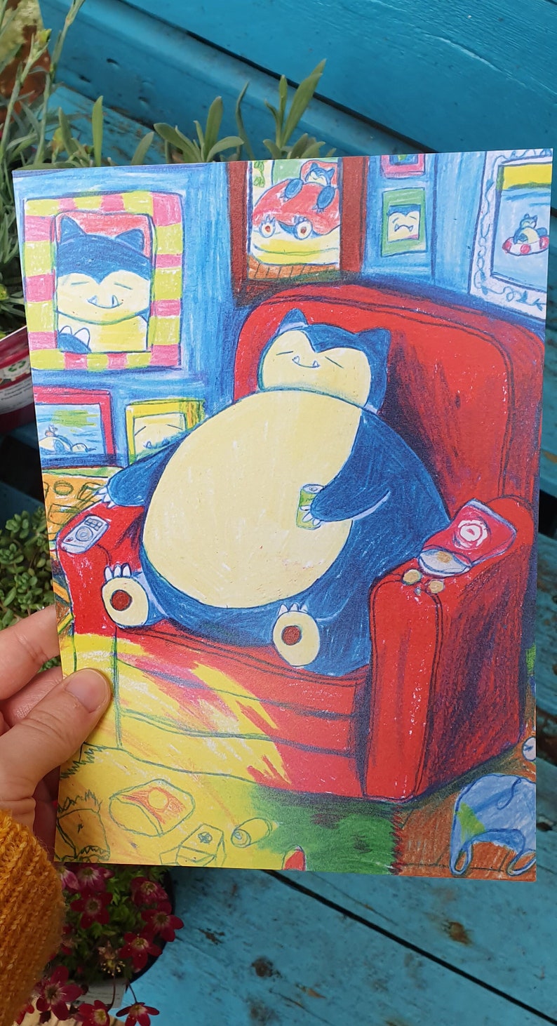 Op de afbeelding: Een kleurrijke illustratie toont een groot, blauw stripfiguur dat ontspant in een rode fauteuil, met een blikje in zijn hand. Het personage is omringd door ingelijste foto's en een rommelige vloer. Het kunstwerk heeft een grillige, cartoonachtige stijl.