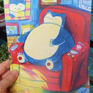 Op de afbeelding: Een kleurrijke illustratie van een stripfiguur, Snorlax, ontspannen in een rode fauteuil. Het personage is blauw en cr&egrave;me, houdt een blikje vast, met snacks en een afstandsbediening in de buurt. Kunstwerk toont ingelijste foto's aan de muur.