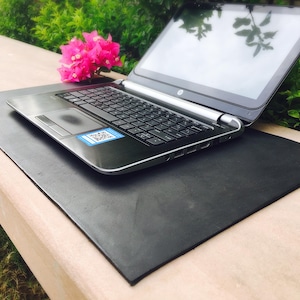 Könnte beinhalten: Ein silber-schwarzer Laptop mit schwarzer Tastatur und einem Touchpad, das einen kleinen blauen quadratischen Aufkleber mit QR-Code aufweist. Der Laptop steht auf einer flachen, rechteckigen schwarzen Matte neben pinkfarbenen Bougainvillea-Blüten.