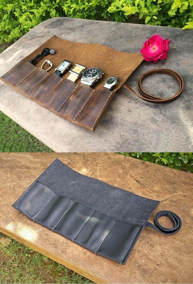 May include: A brown leather watch roll with five compartments, holding several wristwatches. The roll is open, revealing the watches, and has a leather strap for closure. A pink rose is in the background.