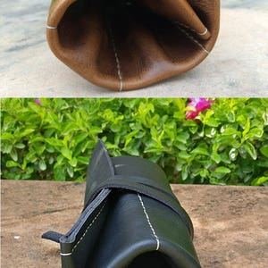 May include: Two leather roll-up cases, one brown and one black, are displayed. The brown case is open, revealing its interior, while the black case is closed and secured with a strap. Both cases have white stitching.