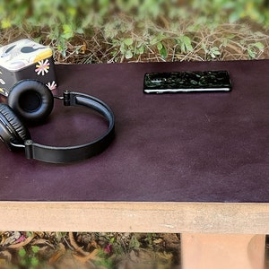 May include: A dark brown leather desk mat with a pair of black headphones, a black smartphone, and a silver watch with a brown leather band.