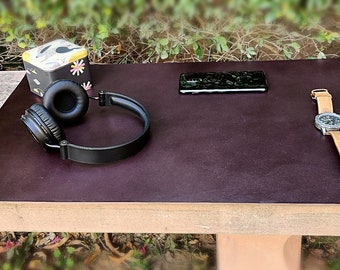 May include: A dark brown leather desk mat with a pair of black headphones, a black smartphone, and a silver watch with a brown leather band.