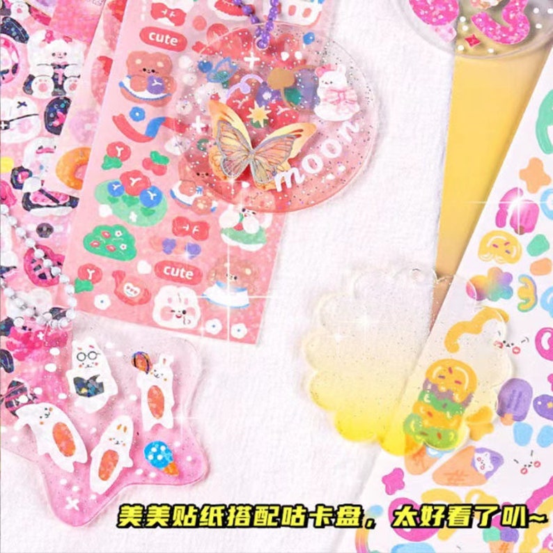 May include: A set of colourful, glittery resin charms with cute cartoon characters and designs. The charms are decorated with stickers featuring butterflies, flowers, and the word "moon".