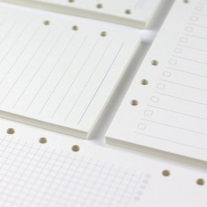 Op de afbeelding: Een set witte papieren navulpagina's voor een disc-gebonden planner. De pagina's hebben verschillende stijlen, waaronder gestreept, geruit en blanco.