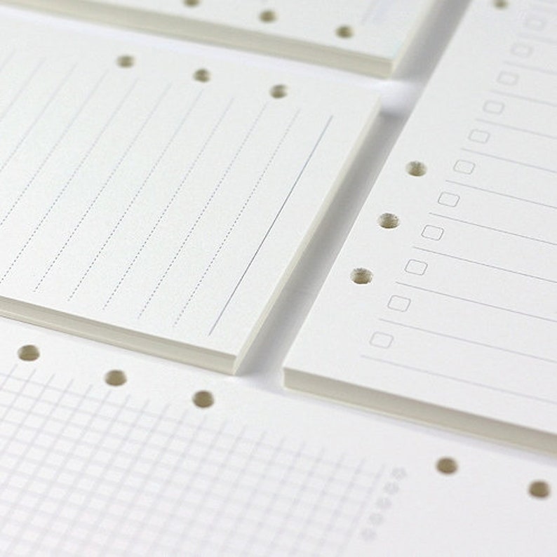 Op de afbeelding: Een set witte papieren navulpagina's voor een disc-gebonden planner. De pagina's hebben verschillende stijlen, waaronder gestreept, geruit en blanco.