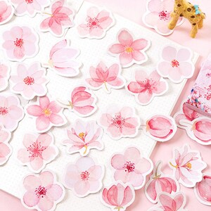 May include: A sheet of pink and white floral stickers with a variety of flower designs. The stickers are in a box with Japanese text that reads "Sakura no Hana".