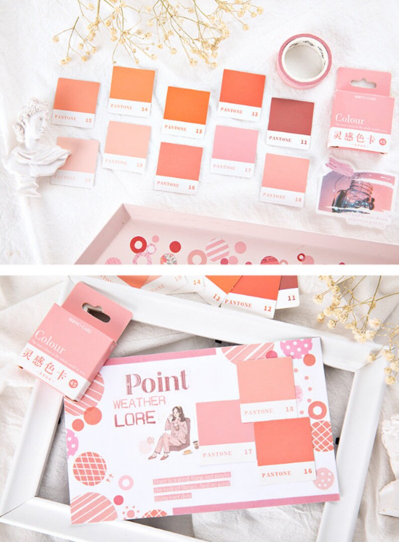 May include: A set of color swatches with the word "PANTONE" and numbers printed on each swatch. The swatches are arranged in a grid pattern on a white surface. The swatches are in shades of pink, orange, and red. The text "Colour 灵感色卡" is printed on a small box.