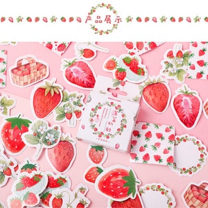 K&ouml;nnte beinhalten: Eine Blatt mit bunten Aufklebern mit Illustrationen von Erdbeeren, Bl&auml;ttern und Blumen. Die Aufkleber befinden sich auf einem rosa Hintergrund. Der Text auf der Aufkleberbox lautet "Strawberry and Cream".