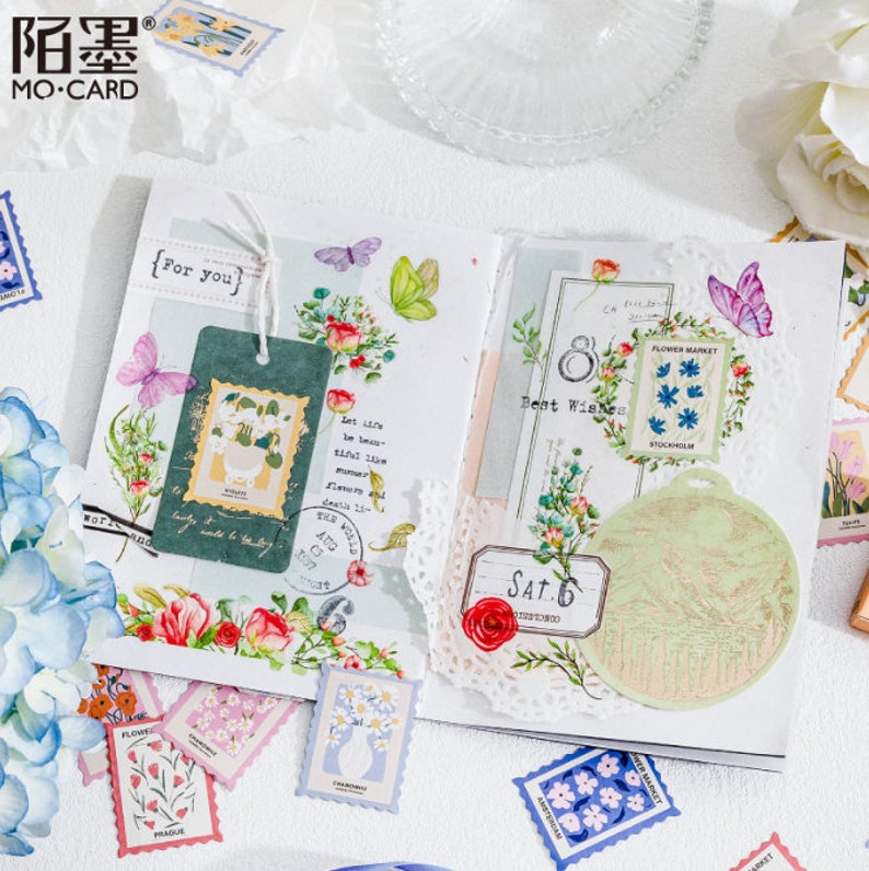 May include: A collection of colorful floral and botanical themed stickers and washi tape. The stickers feature flowers, butterflies, and text like "For You" and "Best Wishes".