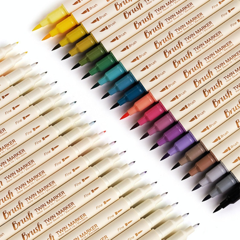 May include: A collection of colorful twin markers with brush and fine tips. The markers are arranged diagonally, showcasing a range of vibrant colors including yellow, green, blue, red, and purple. Each marker is labeled with the text "Brush TWIN MARKER Water Based Ink/Blendable".