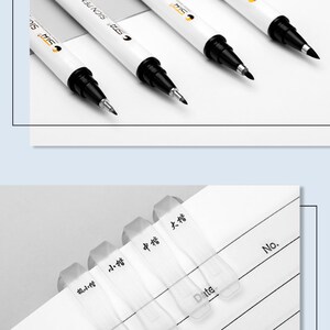 以下が含まれることがあります： 白と黒の細字マーカー4本。白い胴体と黒いキャップ。マーカーには黒い文字で「C.S.P.A. SIGNPEN」とラベルが貼られています。マーカーは白い表面に置かれています。