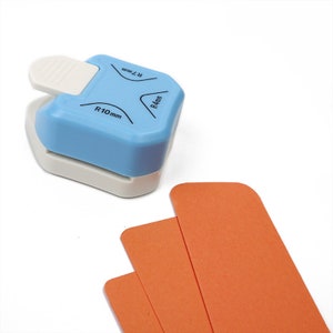 Puede incluir: Un redondeador de esquinas azul y blanco con tres tama&ntilde;os de radio diferentes: R4 mm, R7 mm y R10 mm. El redondeador de esquinas se muestra con tres tiras de papel naranja.