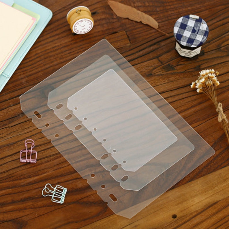 May include: Three clear plastic sheets with rounded corners and six holes down the left side. The sheets are stacked on top of each other, with the largest sheet on the bottom and the smallest sheet on top.