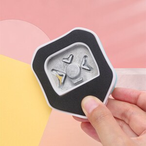 May include: A white and blue paper punch with a black foam pad. The punch has a metal die with a starburst design.