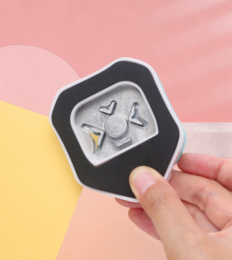 May include: A white and blue paper punch with a black foam pad. The punch has a metal die with a starburst design.