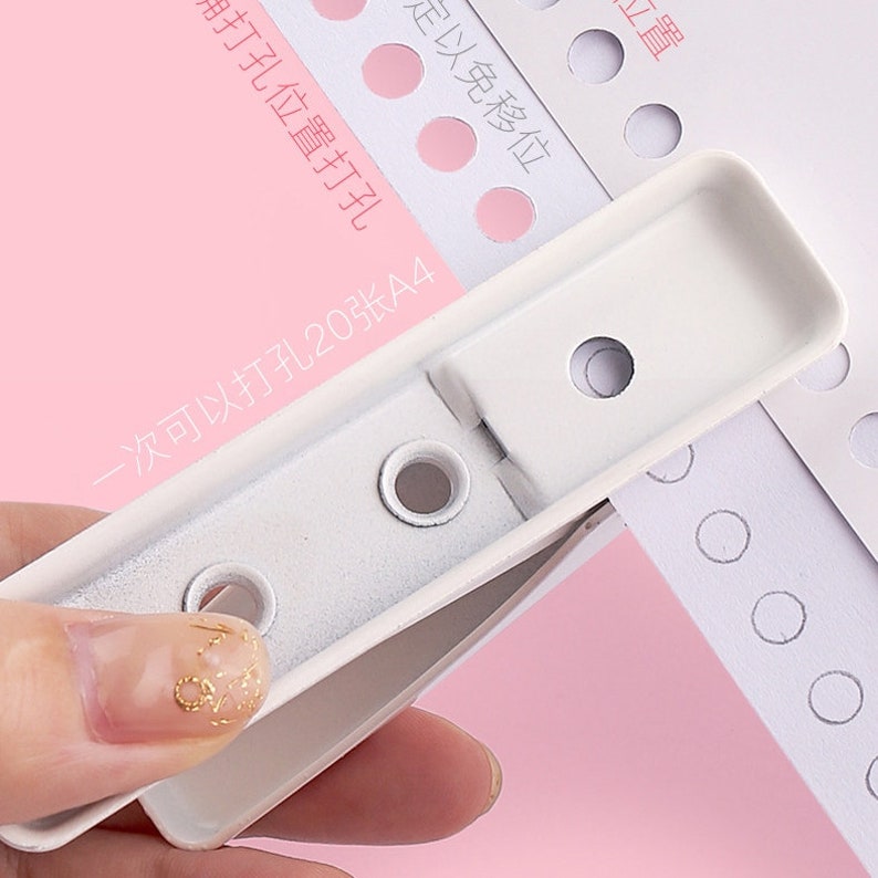 May include: White plastic paper punch with a handle. The punch is designed to punch holes in paper for binding. The text on the paper reads "一次可以打孔20张A4" which translates to "One punch can punch 20 sheets of A4 paper".