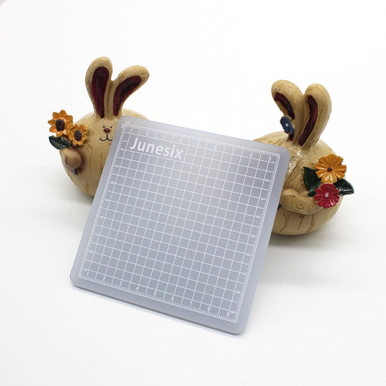 K&ouml;nnte beinhalten: Eine graue, selbstheilende Schneidematte mit einem Gittermuster und dem in Wei&szlig; gedruckten Wort "Junesix". Die Matte ist 23 cm x 23 cm gro&szlig;.