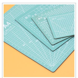 May include: Four self-healing cutting mats in different sizes. The mats are green and have a grid pattern. The largest mat is labeled "A4" and has the dimensions "300 x 220mm". The mats are labeled in Chinese characters.