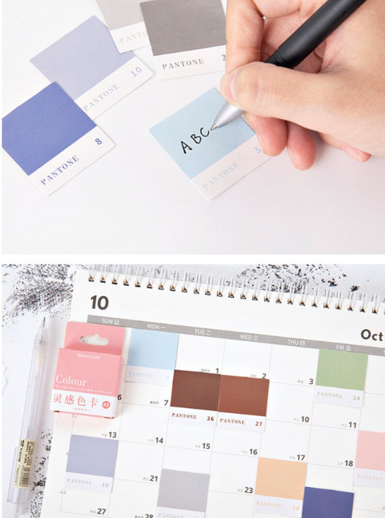 May include: A set of color swatches with the word "PANTONE" printed on each one. The swatches are in various shades of blue, gray, and brown. The swatches are arranged in a grid pattern on a white surface. A hand is writing the letters "A B C" on a light blue swatch.