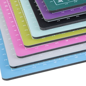 May include: A stack of colorful cutting mats with numbered grids. The mats are layered in a rainbow pattern, starting with a light blue mat at the bottom and ending with a dark green mat at the top.