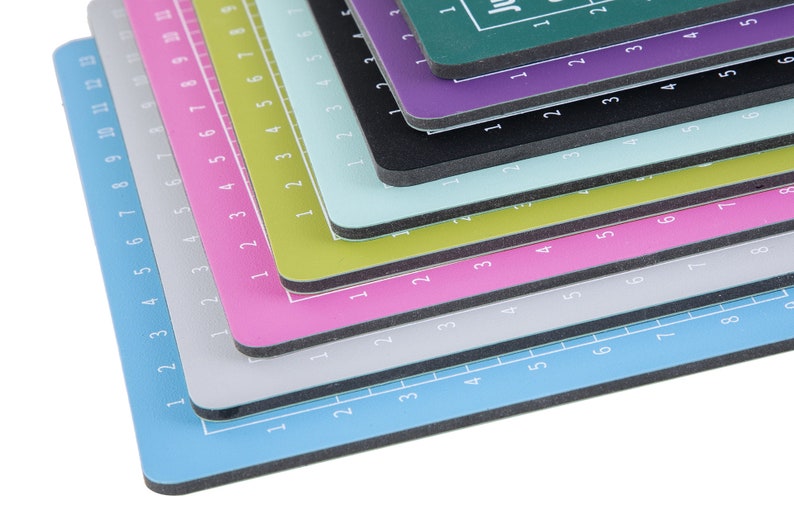 May include: A stack of colorful cutting mats with numbered grids. The mats are layered in a rainbow pattern, starting with a light blue mat at the bottom and ending with a dark green mat at the top.