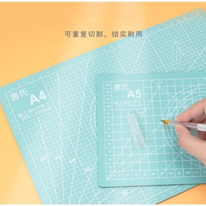 May include: Two green self-healing cutting mats with white grid lines and text. The larger mat is labeled "唐氏 A4 姚工匠DIY手工 300 x 220mm" and the smaller mat is labeled "唐氏 A5 姚工匠DIY手工 220 x 160mm".