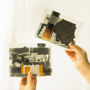 K&ouml;nnte beinhalten: Zwei transparente Plastikh&uuml;llen gef&uuml;llt mit Vintage-Filmstreifen, Fotos und Papierephemera. Die H&uuml;llen haben ein schwarzes Etikett mit dem Text "Exclusive Memory".