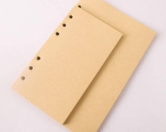 Può includere: Due quaderni di carta marrone con fori perforati lungo il dorso. Il quaderno superiore è leggermente più piccolo del quaderno inferiore.
