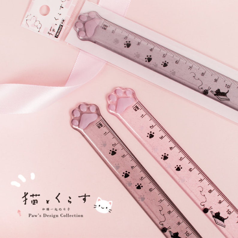 May include: Two pink plastic rulers with paw print designs. The rulers are 10 inches long and have black paw prints and a black cat design at the end. The text "揃いくこす" and "猫とくらす" is printed on the rulers.
