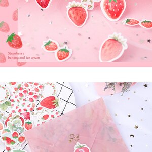 K&ouml;nnte beinhalten: Eine Bogen mit Aufklebern mit Aquarell-Illustrationen von Erdbeeren. Die Aufkleber befinden sich auf einem rosa Hintergrund mit goldenen Glitzersternen. Der Text "Strawberry banana and ice cream" ist auf dem Bogen gedruckt.