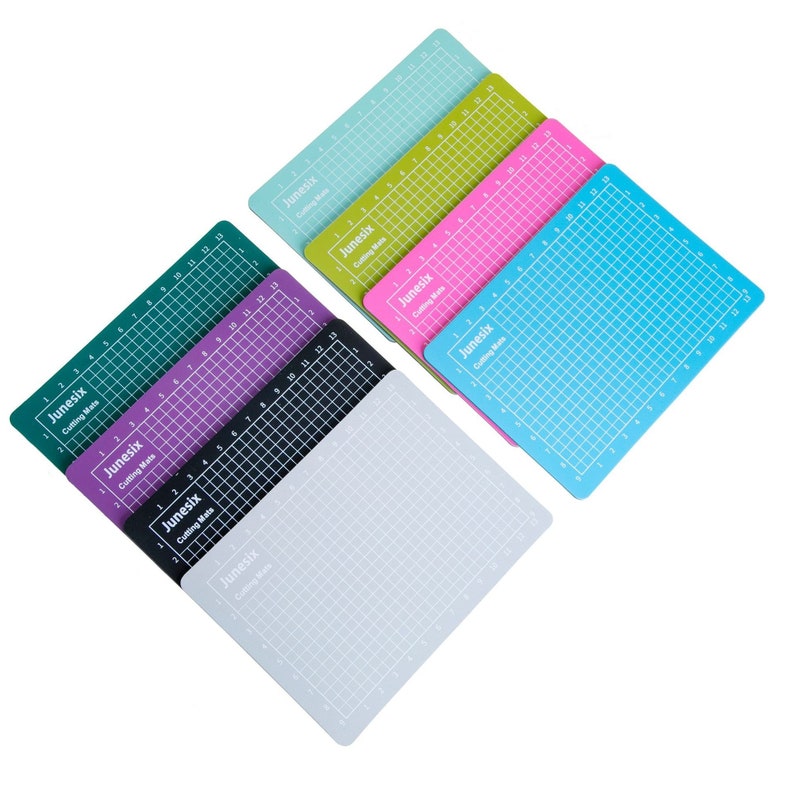 May include: A set of ten self-healing cutting mats in various colors, including green, purple, black, gray, light blue, pink, and yellow. Each mat has a grid pattern and the text "Junesix Cutting Mats" printed on it.