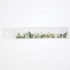 May include: A clear plastic ruler with a floral design. The ruler is 10 inches long and has markings for each inch. The floral design features white daisies, green leaves, and purple flowers.