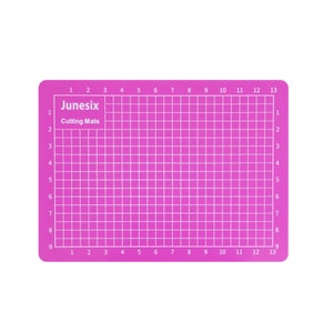 May include: A pink self-healing cutting mat with a grid pattern and numbers 1 through 13 along the top and bottom edges. The mat is labeled "Junesix Cutting Mats".