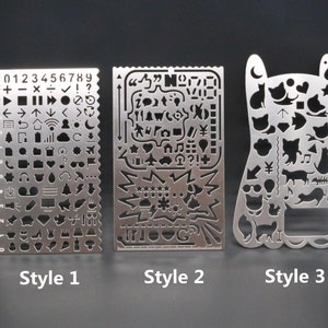 May include: Three metal stencils with different designs. The first stencil has a ruler on the left side and various symbols and numbers on the right side. The second stencil has a variety of symbols and designs. The third stencil has a cat-shaped design with various cat-related symbols.