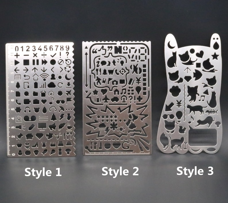 May include: Three metal stencils with different designs. The first stencil has a ruler on the left side and various symbols and numbers on the right side. The second stencil has a variety of symbols and designs. The third stencil has a cat-shaped design with various cat-related symbols.