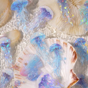 May include: A collection of iridescent blue jellyfish stickers on a white seashell background. The stickers have a holographic finish and are arranged in a cluster.