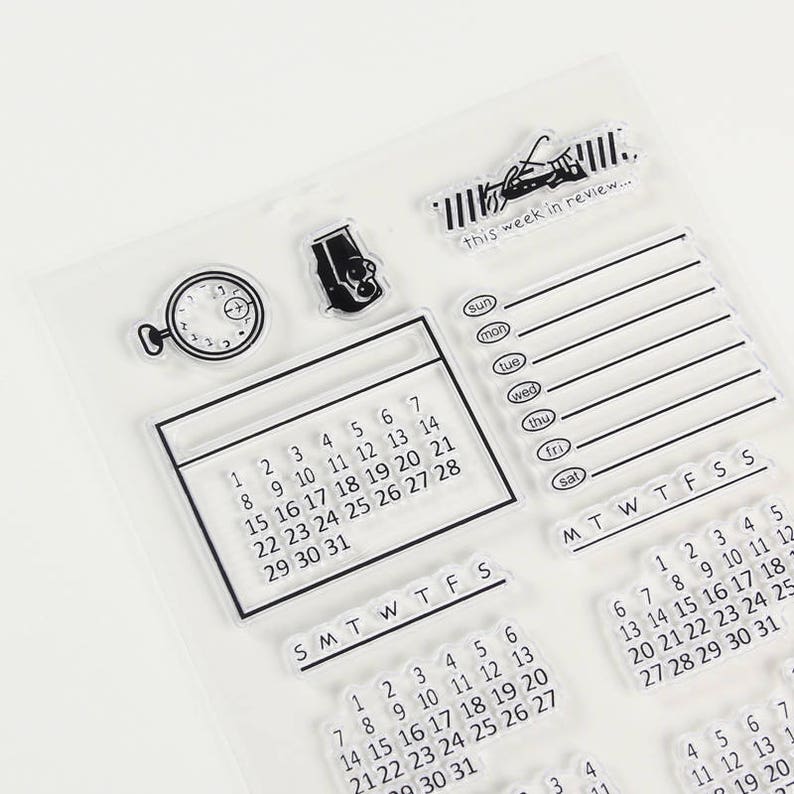 Pu&ograve; includere: Set di timbri trasparenti con vari elementi di calendario e pianificazione. Include una griglia del calendario, un banner di revisione settimanale, un orologio e un'icona della fotocamera. Il testo "this week in review..." &egrave; visibile.