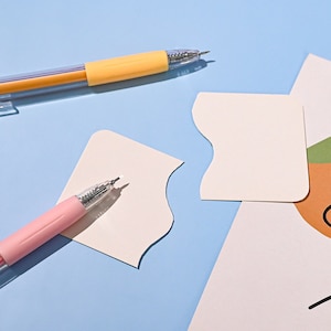Puede incluir: Dos notas adhesivas blancas con bordes ondulados sobre un fondo azul claro. Tambi&eacute;n hay un bol&iacute;grafo rosa y uno amarillo sobre la superficie.