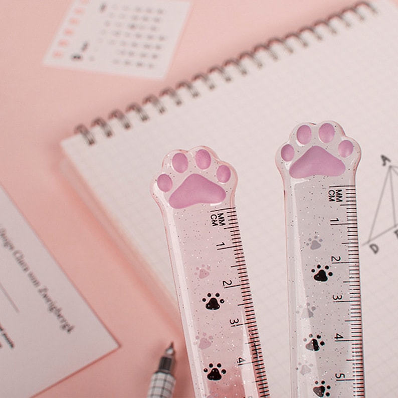 May include: Two pink glitter rulers with paw print designs. The rulers are 12.7 cm long and have markings in both centimetres and millimetres.