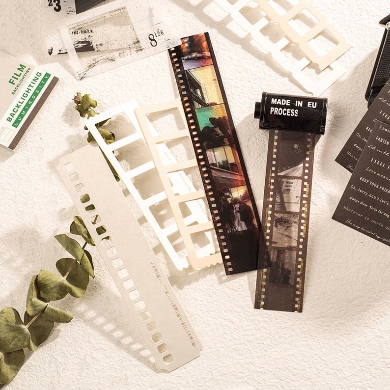 K&ouml;nnte beinhalten: Ein Satz von Filmstreifen-Aufklebern im Vintage-Stil in Braun und Wei&szlig;. Die Aufkleber zeigen Bilder von einem Geb&auml;ude, einem Paar und einer Br&uuml;cke. Die Aufkleber enthalten auch den Text "MADE IN EU PROCESS".