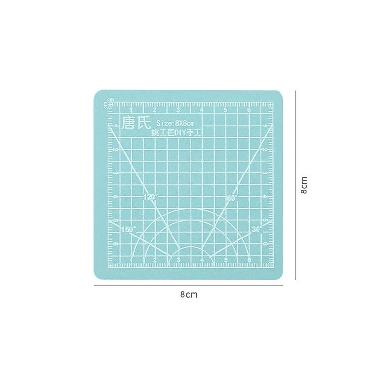 May include: A light blue self-healing cutting mat with a grid pattern and a protractor. The mat is 8 inches by 8 inches and has the text "唐氏 Size:8X8cm 姚工匠DIY手工" printed on it.