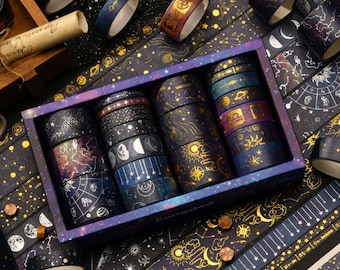 Puede incluir: Un conjunto de 12 cintas washi con diseños celestiales y galácticos. Las cintas son negras con detalles dorados y presentan estrellas, lunas, planetas y constelaciones. Las cintas están empaquetadas en una caja azul con un estampado de galaxia.