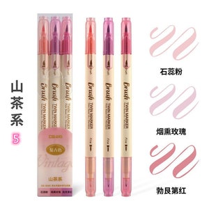 May include: A set of five dual-tip brush markers in shades of pink and peach. The markers are labeled "Brush Twin Marker" and "Fine". The packaging includes the text "Vintage" and Chinese characters. Swatches of the marker colors are displayed.
