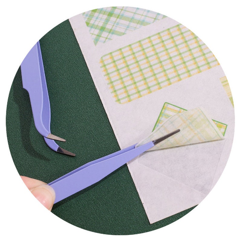 Op de afbeelding: Twee pincetten, een blauwe en een zilveren, worden gebruikt om een ​​vel gepatenteerd papier te verwijderen. Het papier heeft een geruit patroon in groen, geel en wit.