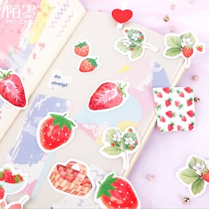 K&ouml;nnte beinhalten: Ein Bogen mit bunten Aufklebern mit Aquarell-Illustrationen von Erdbeeren, Blumen und einem Korb mit Erdbeeren. Die Aufkleber sind auf wei&szlig;em Hintergrund und haben eine verspielte, niedliche &Auml;sthetik.