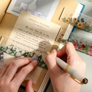 May include: A close-up of a hand using a clear ruler with floral designs to measure a page of a book. The book is open to a page with text from the book "Frederick Buechner". The text reads, "He said, "One life on this earth is all that we get, whether it is enough or not enough, and the obvious conclusion would seem to be that at the very least we are as if we do not live it fully".