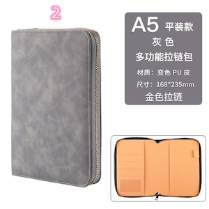 K&ouml;nnte beinhalten: Graues A5-Portfolio mit goldenem Rei&szlig;verschluss und strukturierter Oberfl&auml;che. Das Innere ist beige mit Kartenf&auml;chern und einer Tasche. Die Abmessungen betragen 16,8 cm x 23,5 cm.